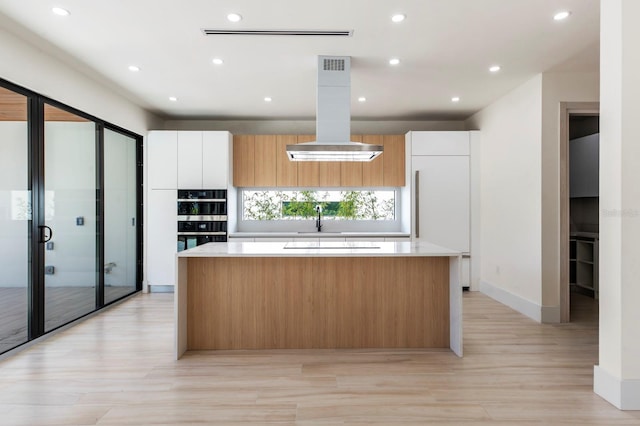 kitchen featuring a center island, double oven, island range hood, white cabinetry, and light hardwood / wood-style floors