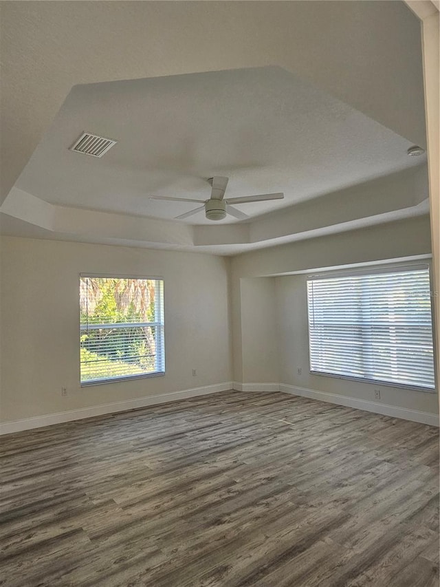 empty room with a raised ceiling, ceiling fan, and hardwood / wood-style floors