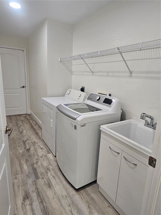 washroom with sink, washing machine and dryer, cabinets, and light wood-type flooring