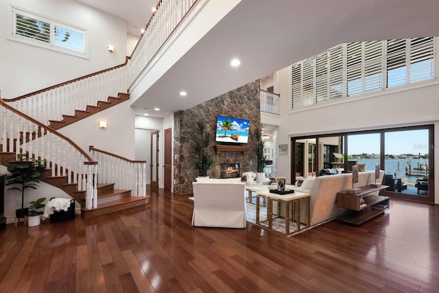 living room featuring a high ceiling, a water view, a stone fireplace, and dark hardwood / wood-style floors