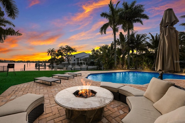 pool at dusk with a patio area, a water view, and a fire pit