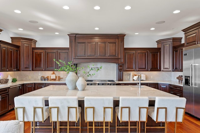 kitchen with a kitchen island with sink, stainless steel appliances, a kitchen breakfast bar, and dark brown cabinetry