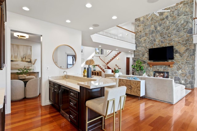 kitchen featuring a stone fireplace, a breakfast bar, sink, dark brown cabinets, and hardwood / wood-style flooring