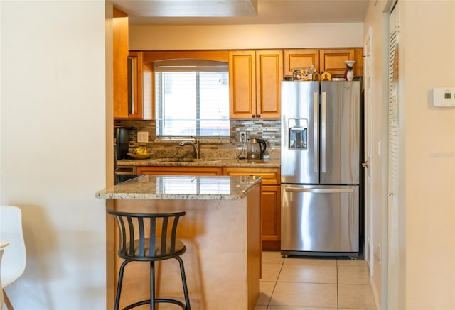 kitchen with light stone countertops, sink, tasteful backsplash, stainless steel fridge with ice dispenser, and a breakfast bar