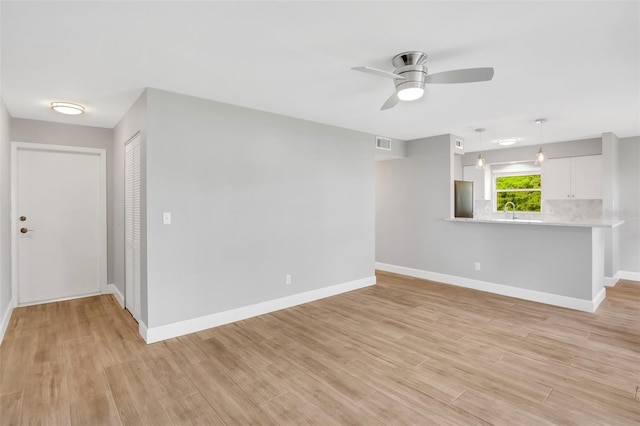 unfurnished living room featuring light wood-type flooring, ceiling fan, and sink