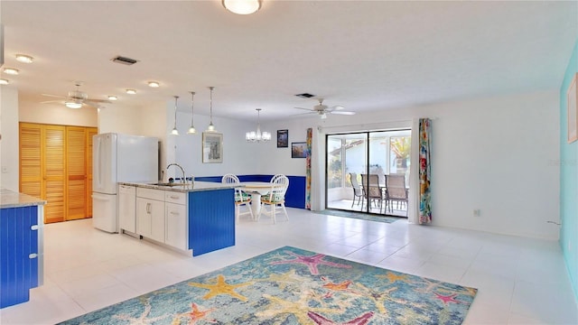 kitchen with sink, hanging light fixtures, an island with sink, white fridge, and white cabinetry