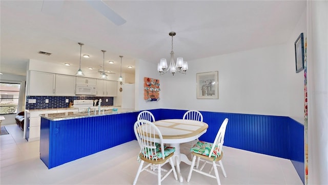 kitchen with kitchen peninsula, hanging light fixtures, decorative backsplash, light stone counters, and white cabinetry