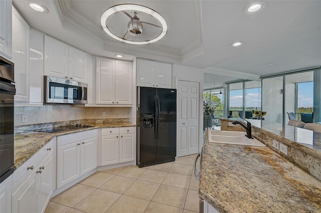 kitchen with white cabinets, light stone countertops, black appliances, a tray ceiling, and tasteful backsplash