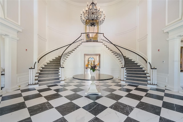 interior space featuring dark tile floors, a notable chandelier, a high ceiling, decorative columns, and crown molding