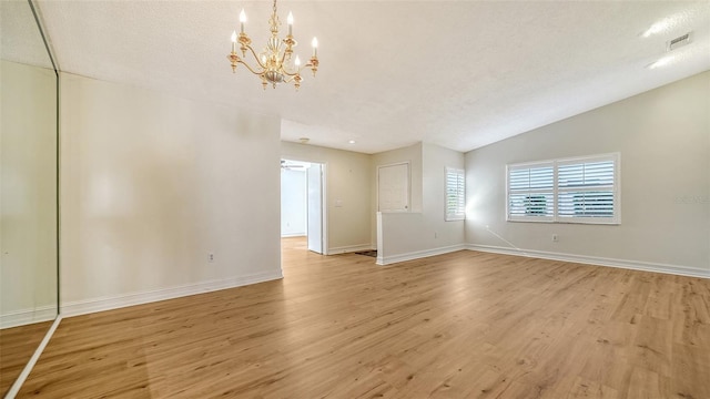 empty room featuring a textured ceiling, a chandelier, light hardwood / wood-style floors, and vaulted ceiling