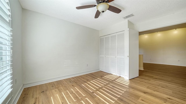 unfurnished bedroom featuring ceiling fan, a closet, light hardwood / wood-style floors, and a textured ceiling