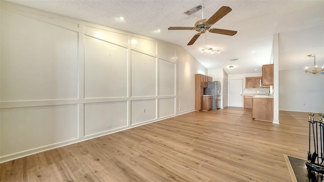 unfurnished living room featuring ceiling fan with notable chandelier, a textured ceiling, light hardwood / wood-style flooring, and vaulted ceiling