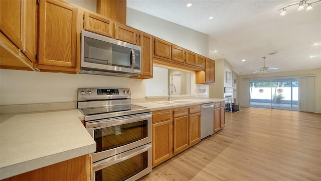 kitchen featuring appliances with stainless steel finishes, vaulted ceiling, ceiling fan, sink, and light hardwood / wood-style floors