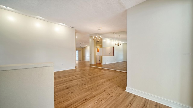 spare room with a notable chandelier, light hardwood / wood-style floors, and a textured ceiling