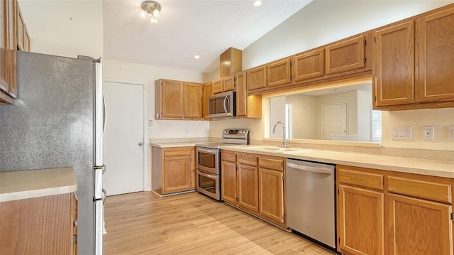 kitchen featuring appliances with stainless steel finishes, light wood-type flooring, a textured ceiling, sink, and lofted ceiling