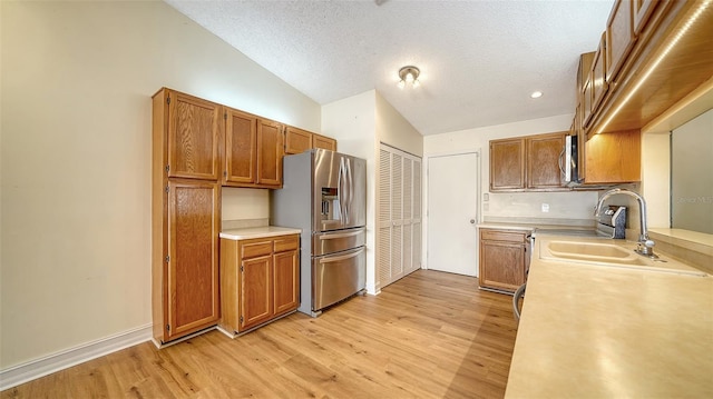 kitchen featuring sink, a textured ceiling, vaulted ceiling, appliances with stainless steel finishes, and light wood-type flooring