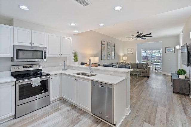 kitchen with light hardwood / wood-style floors, appliances with stainless steel finishes, sink, white cabinets, and kitchen peninsula