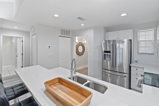 kitchen with high quality fridge, white cabinetry, sink, kitchen peninsula, and a breakfast bar