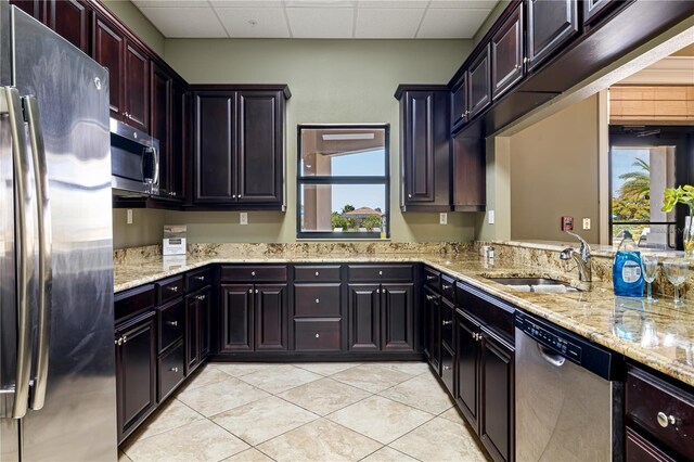 kitchen with stainless steel appliances, light tile floors, sink, and light stone countertops