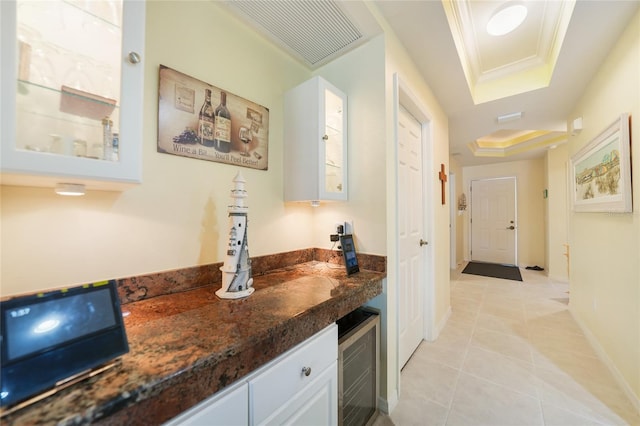 corridor featuring light tile floors, a tray ceiling, beverage cooler, and crown molding