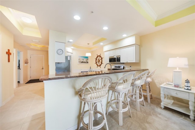 kitchen with kitchen peninsula, a raised ceiling, refrigerator, a kitchen bar, and white cabinets