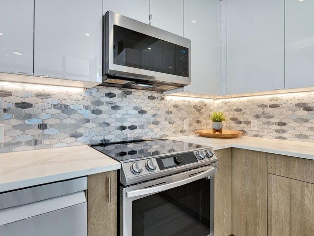 kitchen with white cabinets, light stone counters, appliances with stainless steel finishes, and tasteful backsplash