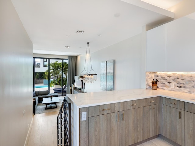 kitchen featuring pendant lighting, backsplash, light hardwood / wood-style flooring, light stone countertops, and kitchen peninsula