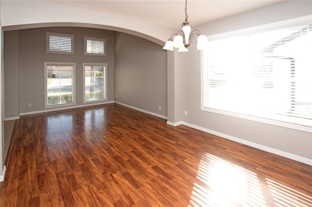 spare room with dark hardwood / wood-style floors and an inviting chandelier