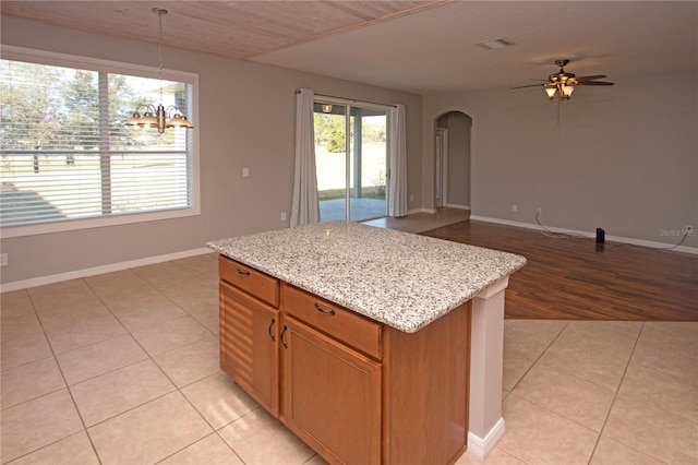 kitchen featuring pendant lighting, light tile patterned floors, a center island, light stone counters, and ceiling fan with notable chandelier