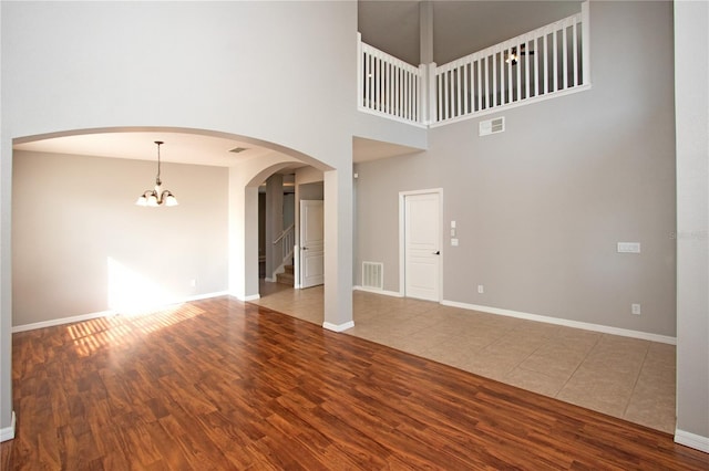 unfurnished living room featuring wood-type flooring, a chandelier, and a high ceiling