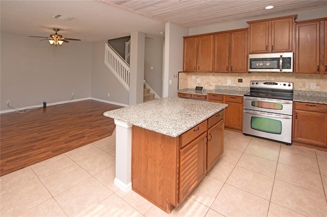 kitchen featuring light tile patterned floors, ceiling fan, stainless steel appliances, a center island, and decorative backsplash