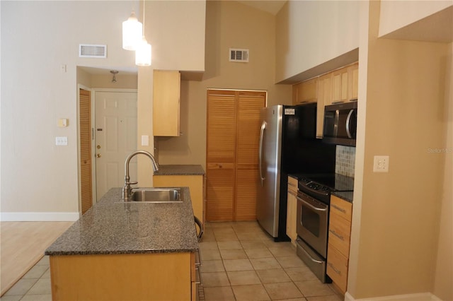 kitchen featuring sink, light tile flooring, decorative light fixtures, stainless steel appliances, and dark stone countertops