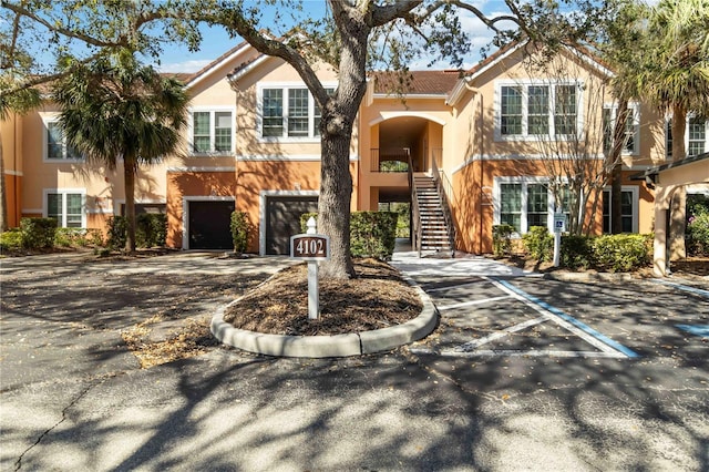 multi unit property featuring a tile roof, stucco siding, an attached garage, and stairs