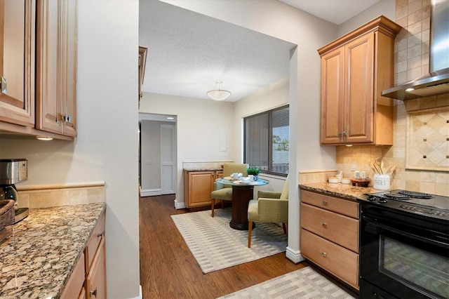 kitchen featuring light stone counters, wall chimney exhaust hood, tasteful backsplash, black range with electric stovetop, and dark hardwood / wood-style flooring