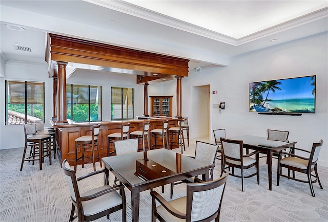 carpeted dining space featuring ornamental molding, bar area, and decorative columns