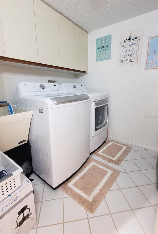 laundry room featuring cabinets, a textured ceiling, washing machine and dryer, and light tile patterned flooring