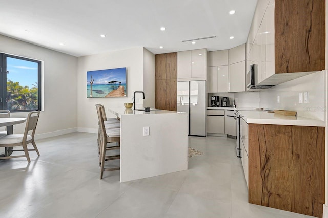 kitchen with a center island with sink, backsplash, built in fridge, a breakfast bar, and sink