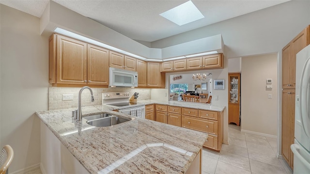 kitchen featuring white appliances, kitchen peninsula, sink, light tile flooring, and a skylight