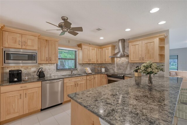 kitchen with light brown cabinets, wall chimney range hood, stainless steel appliances, ceiling fan, and light tile floors