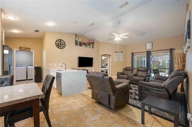 living room featuring vaulted ceiling, washer and clothes dryer, ceiling fan, sink, and light tile floors