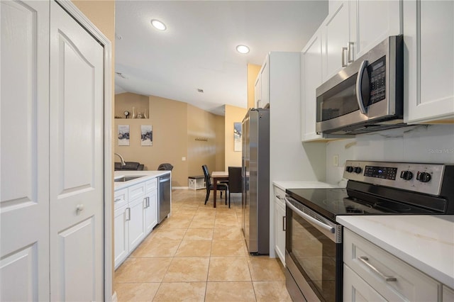 kitchen featuring appliances with stainless steel finishes, white cabinetry, light tile flooring, and vaulted ceiling