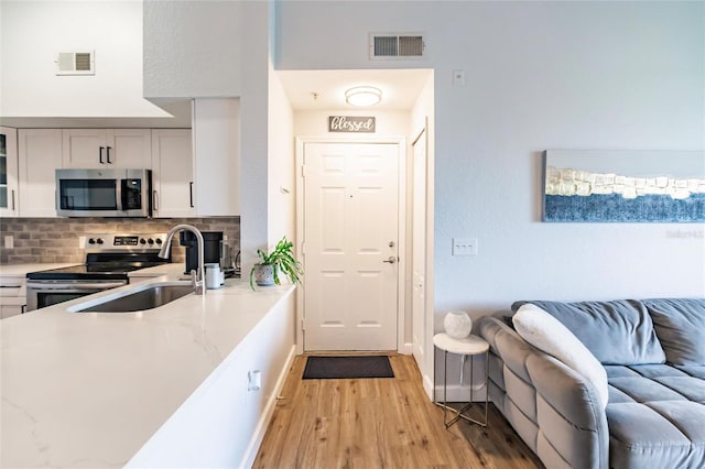 kitchen with white cabinetry, light wood-type flooring, stainless steel appliances, light stone counters, and backsplash