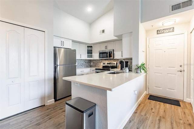 kitchen with kitchen peninsula, light wood-type flooring, high vaulted ceiling, appliances with stainless steel finishes, and sink