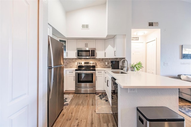 kitchen with high vaulted ceiling, tasteful backsplash, light hardwood / wood-style flooring, and stainless steel appliances