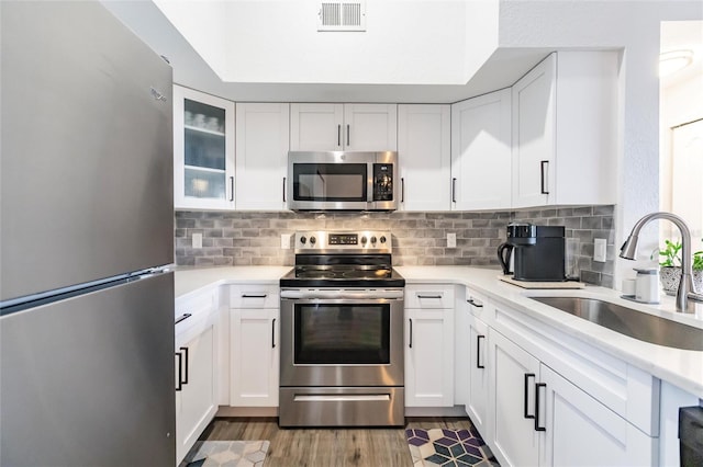 kitchen with stainless steel appliances, backsplash, light wood-type flooring, white cabinets, and sink