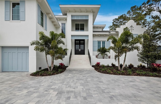 entrance to property featuring french doors, stucco siding, a garage, and decorative driveway