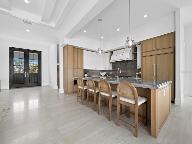 kitchen featuring premium range hood, tasteful backsplash, brown cabinetry, a breakfast bar area, and french doors