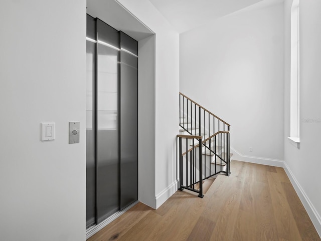 hall with elevator, wood finished floors, baseboards, and an upstairs landing