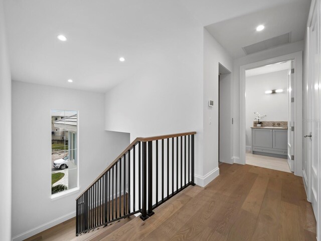 hallway with an upstairs landing, wood finished floors, baseboards, and recessed lighting
