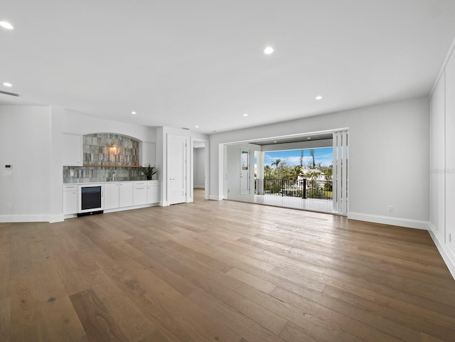 unfurnished living room with wine cooler, hardwood / wood-style flooring, baseboards, recessed lighting, and a sink